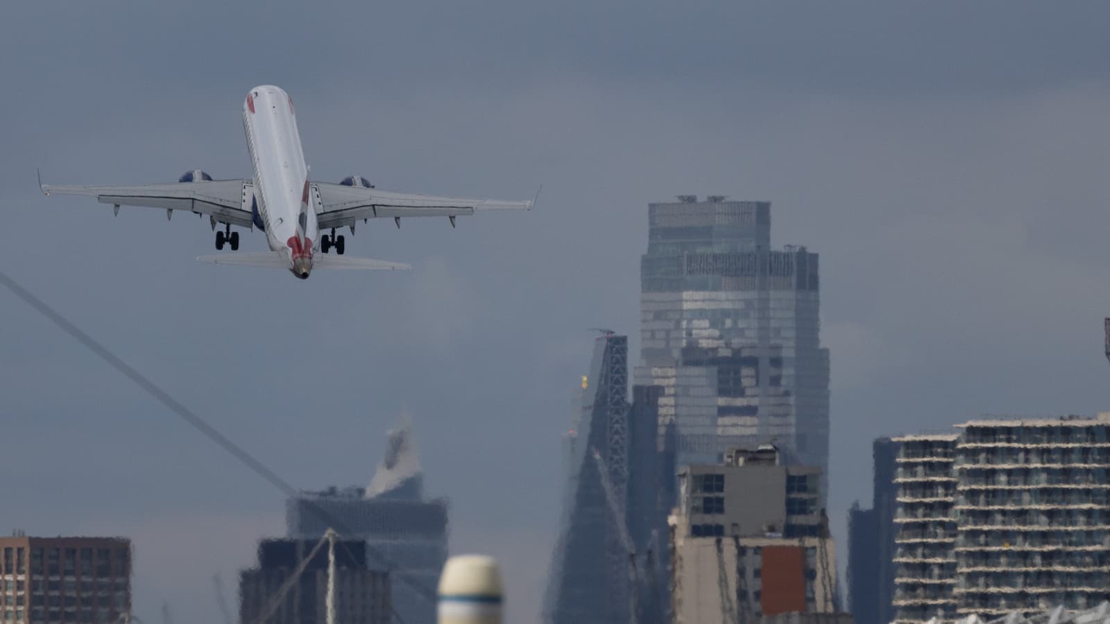 A passenger aircraft, operated by British Airways, takes off from London City Airport Ltd. in view of the city of London in London, UK