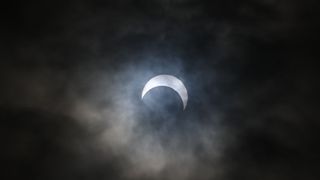 partial eclipse through clouds. The sun appears to take a crescent shape as the moon appears to take a "bite" out of the sun.