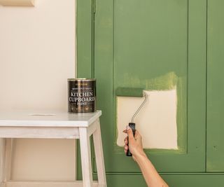 hand using roller to paint kitchen cabinet door green