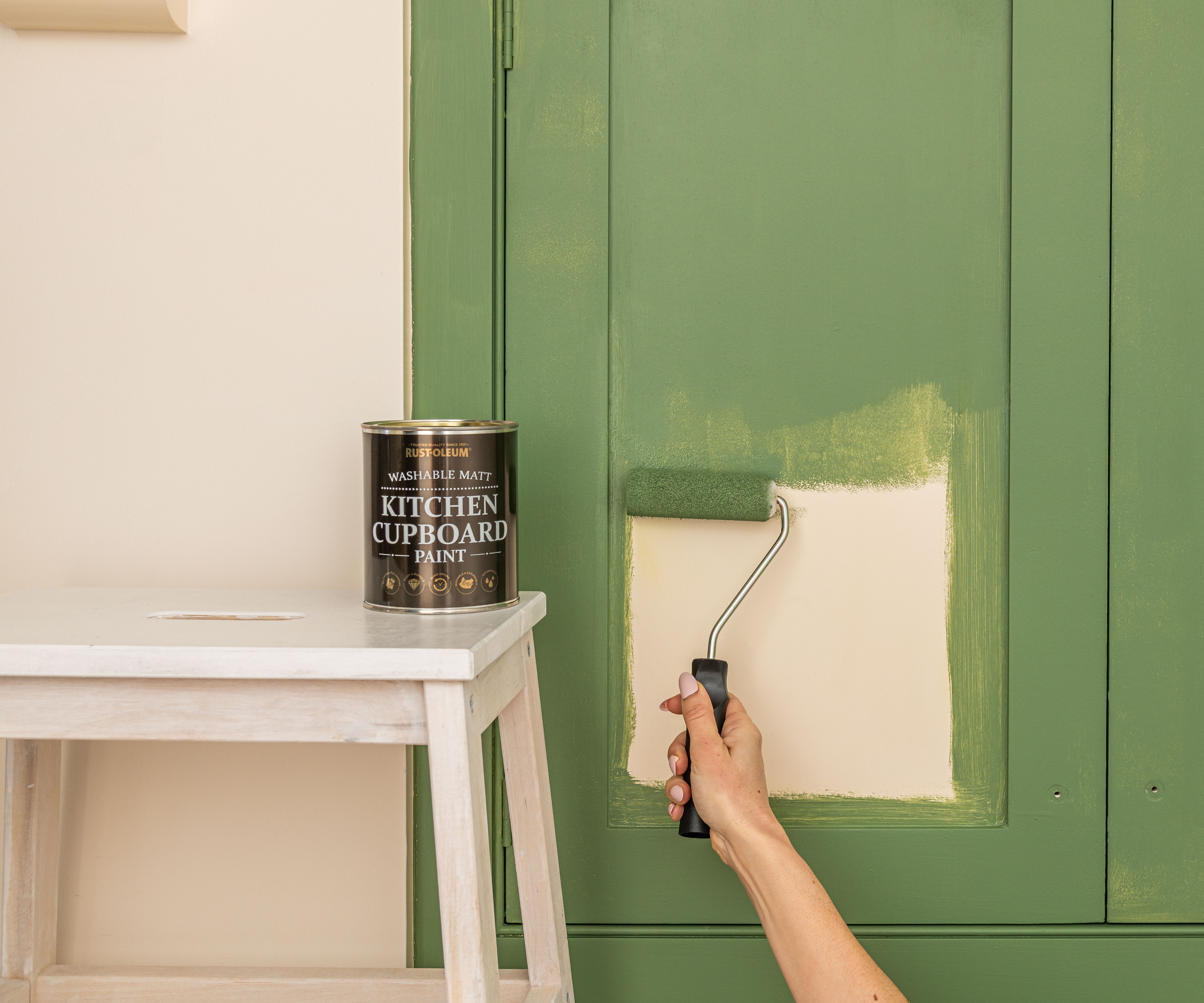 hand using roller to paint kitchen cabinet door green