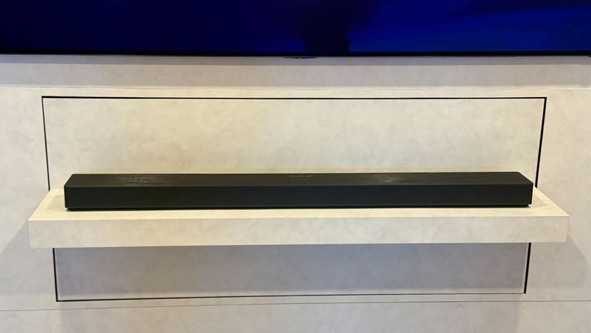 Samsung's HW-QS90H sitting below a wall-mounted TV on a white backdrop