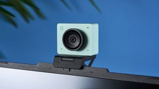 a photograph of a 1 inch wide mint webcam with a 4K sensor and built-in microphone, photographed against a blue background