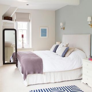 Small bedroom painted cream with a sage feature wall, double bed and full length mirror visible