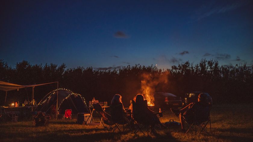 Rear view of a group of people spending time together, sitting in camping chairs around a burning camp fire in camping field