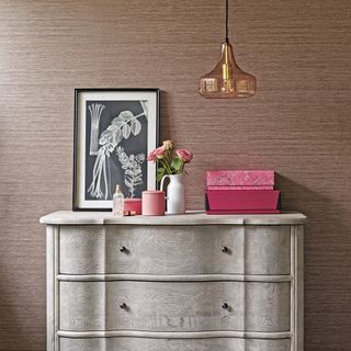 Wooden chest of drawers in front of textured wallpaper with glass pendant light