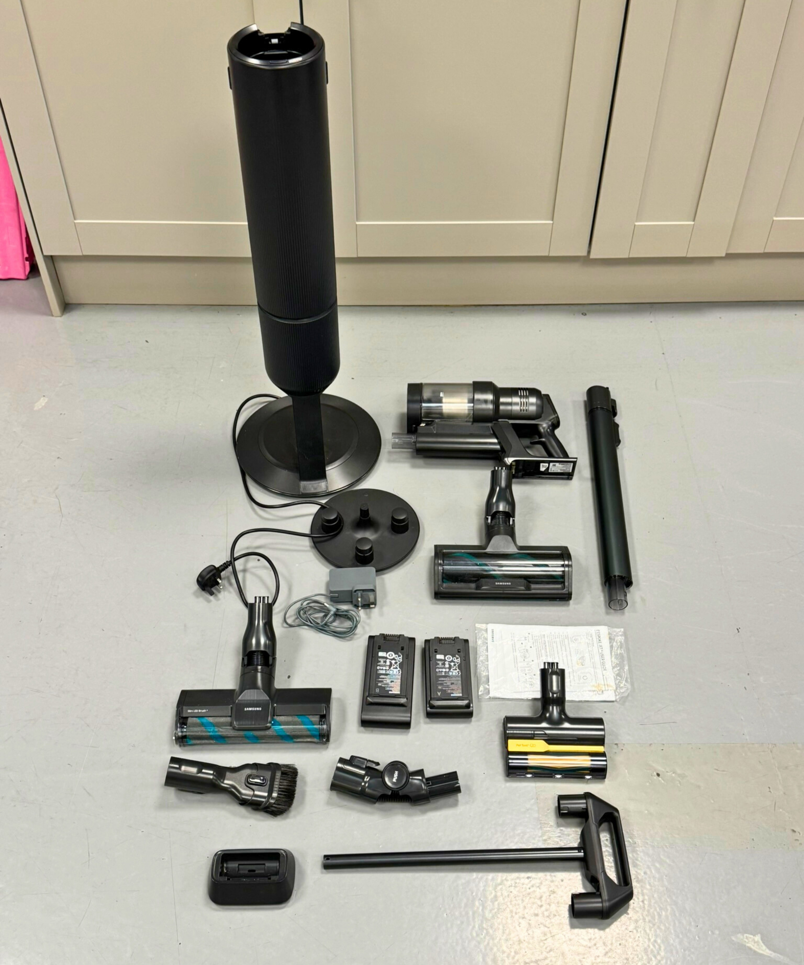 All parts and attachments of the Samsung Bespoke AI Jet Ultra laid out on gray floor.