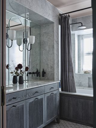 Bathroom with double sink, marbled walls and showerhead over the bath. A replanned and redesigned apartment in West London, in an art deco mansion, home of Emily Maynard and Ron Totton and their family
