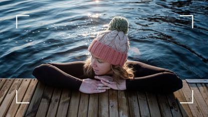Woman holding onto the side of a deck wearing woolly hat with body in cold water, exploring the benefits of cold water swimming
