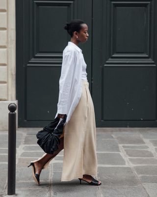 fashion influencer Sylvie Mus on the streets of Paris wearing a spring outfit with a white button-down shirt