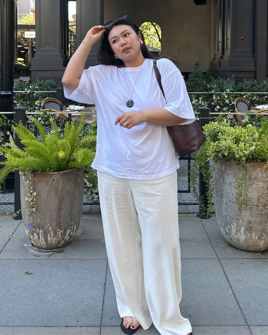 @marina_torres wears a white t-shirt, cream wide-leg trousers, jelly flip flops and a burgundy leather tote
