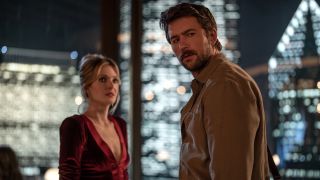 Meghann Fahy and Brandon Sklenar looking over while standing up in restaurant with Chicago view in the background
