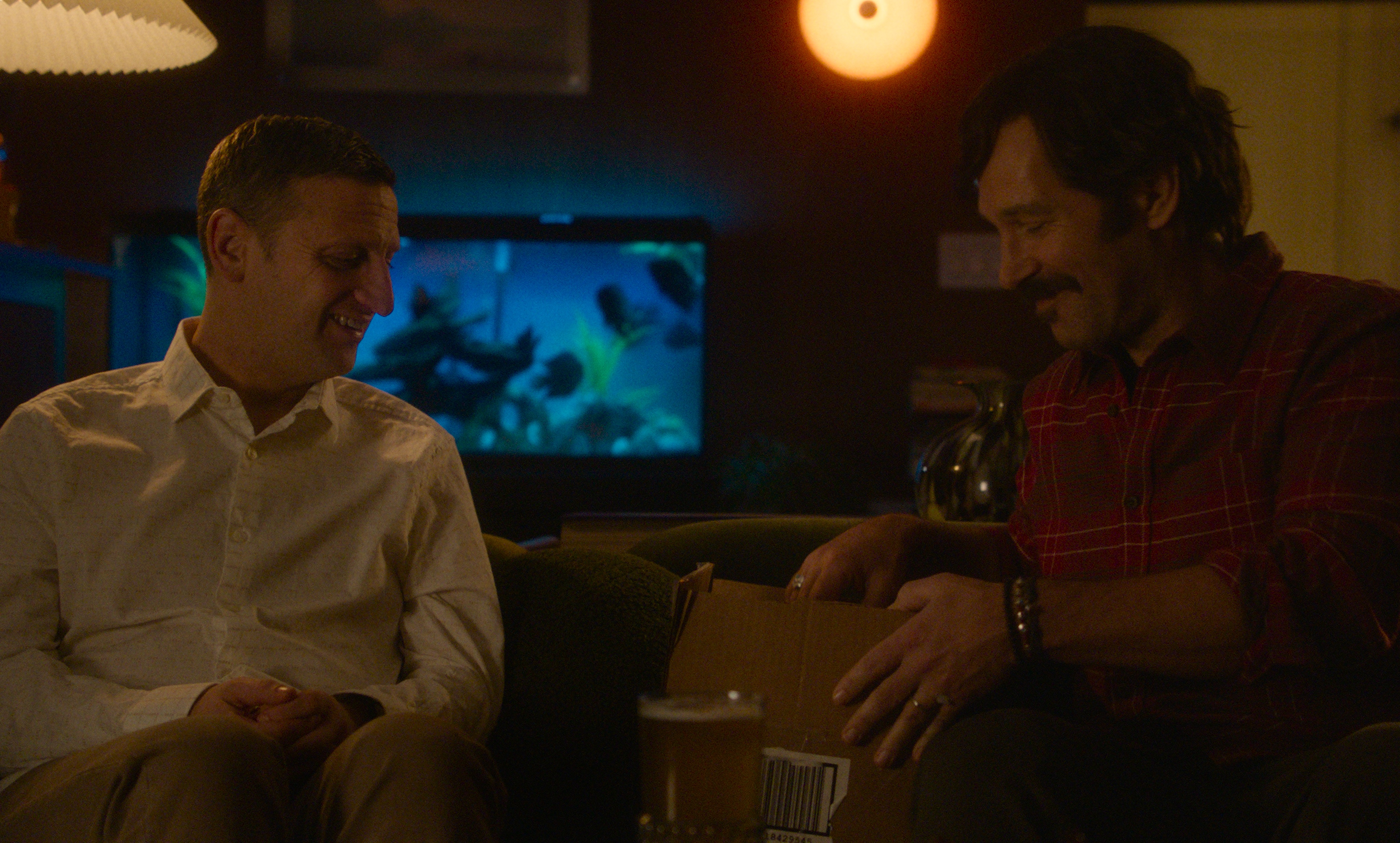 tim robinson as craig and paul rudd as austing sitting on a couch opening a package in the movie friendship
