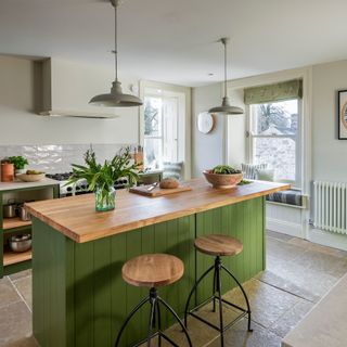 Green kitchen with wooden topped island and window seats