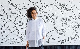 Artist Shantell Martin standing in front of her art piece for Max Mara. Art is of black lines on white canvas, that represent faces.