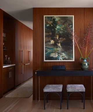 A room with wooden paneled walls and two vintage stools in front of a framed piece of artwork