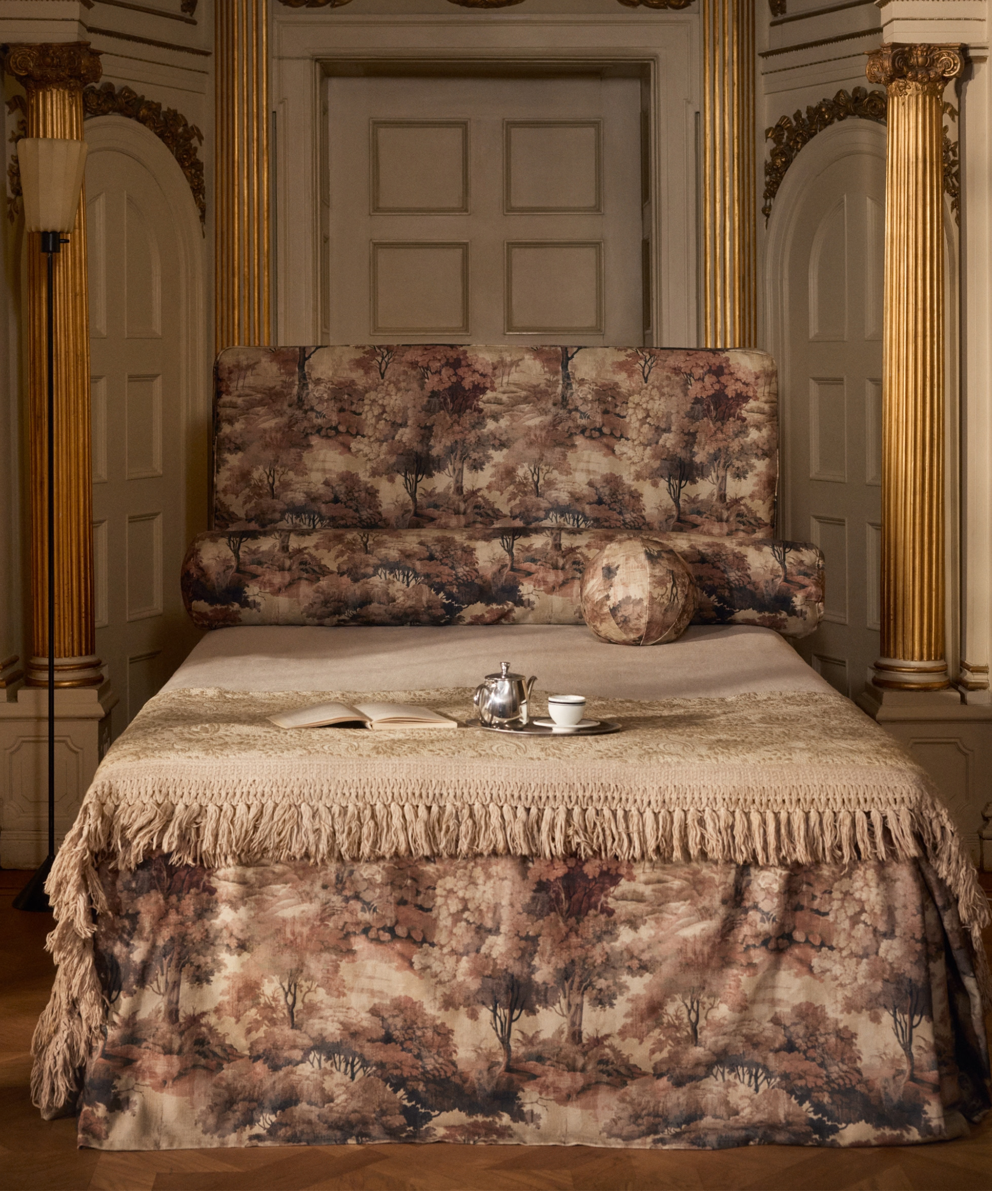 Tapestry-drenched bedscape topped with a bullion fringe-edged throw blanket in an opulent European room