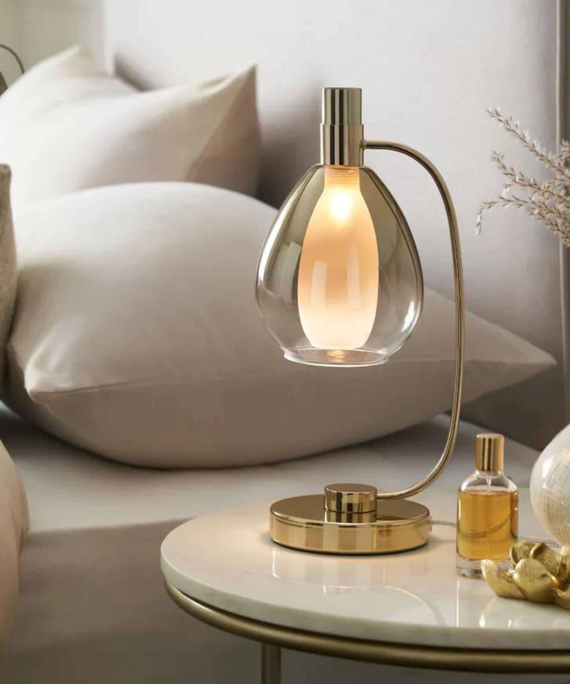 Elegant bedside table lamp with a curved glass shade and gold base, casting a warm, ambient glow for a cosy bedroom atmosphere.