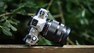 Olympus M.Zuiko 12‑40mm f/2.8 Pro lens on a wooden surface in front of green foliage