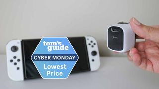 The Genki Covert Dock Mini in hand next to a Nintendo Switch OLED with a Tom's Guide Cyber Monday deals badge