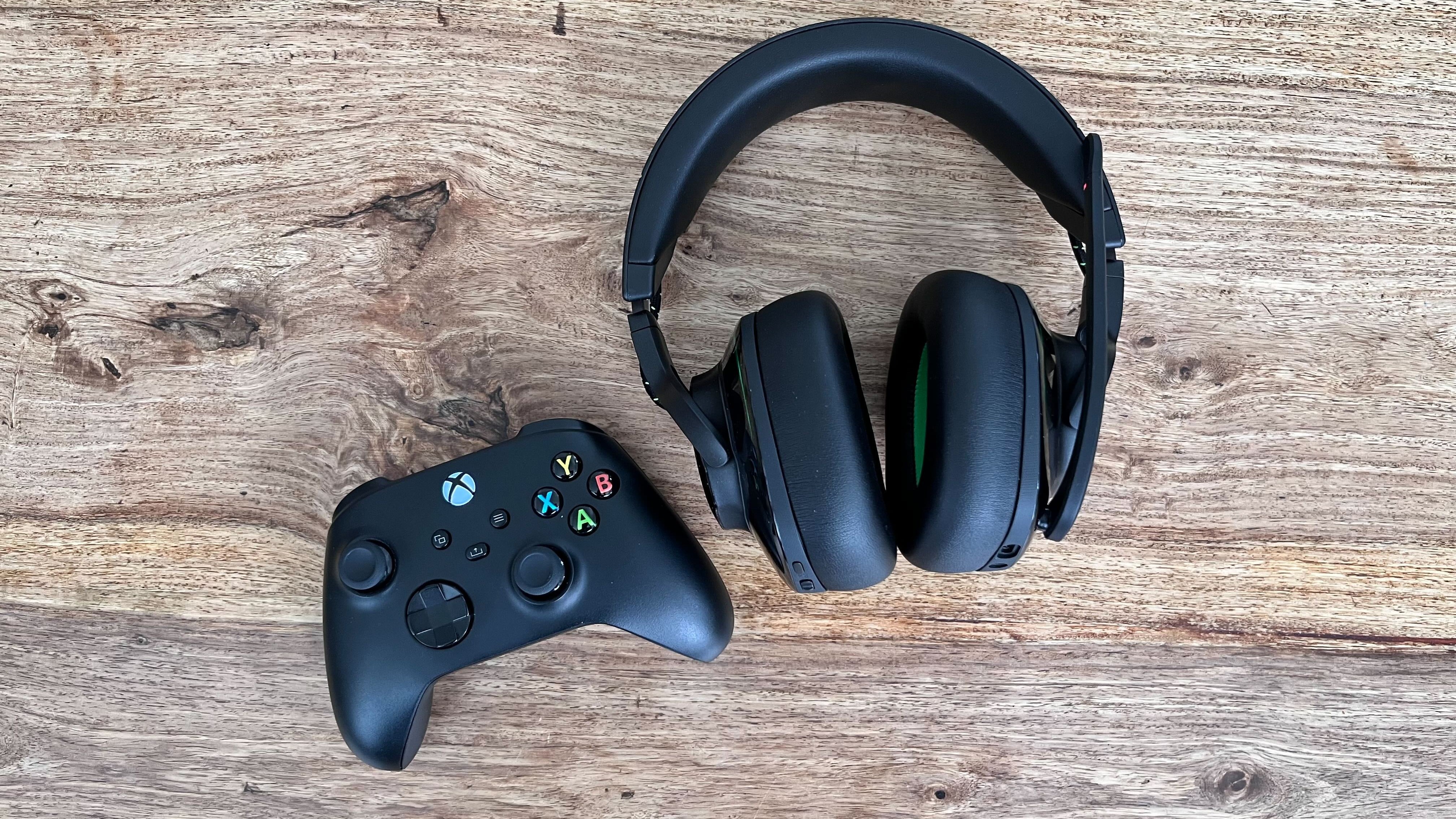 The JBL Quantum 910X on a wooden table placed next to a black Xbox controller.