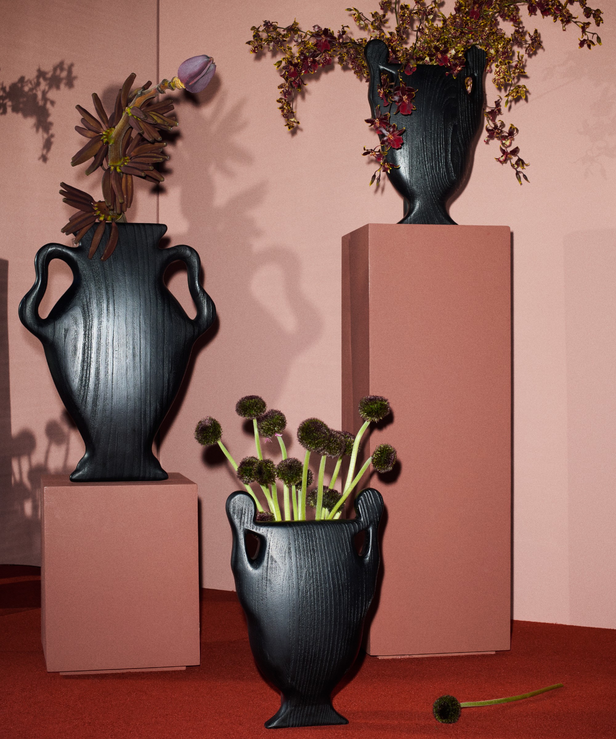 Three of the Cyma vases from the H&amp;amp;M Home x Kelly Wearstler collection filled with flowers and placed on pink pillars set against a pink wall
