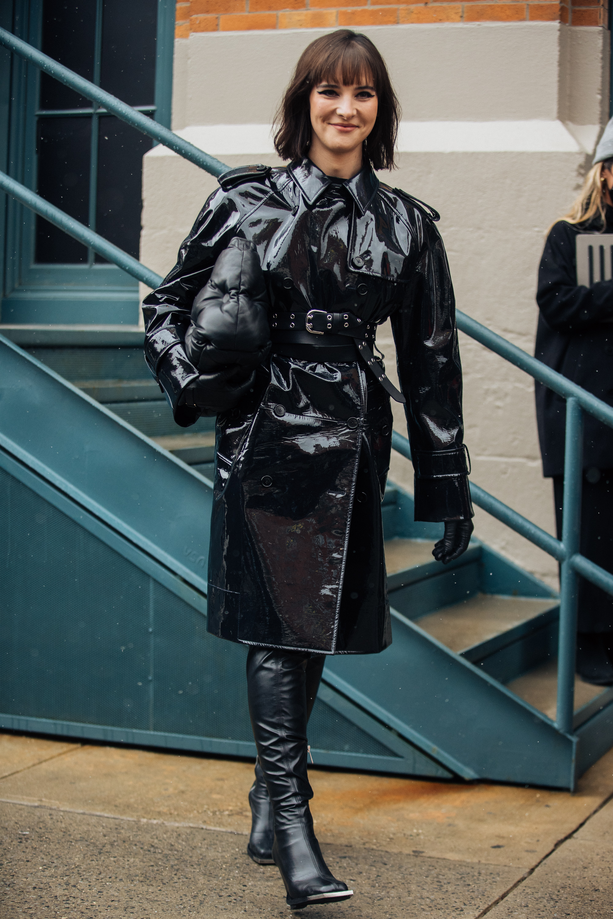 a woman wearing a patent leather trench coat with leather boots in street style