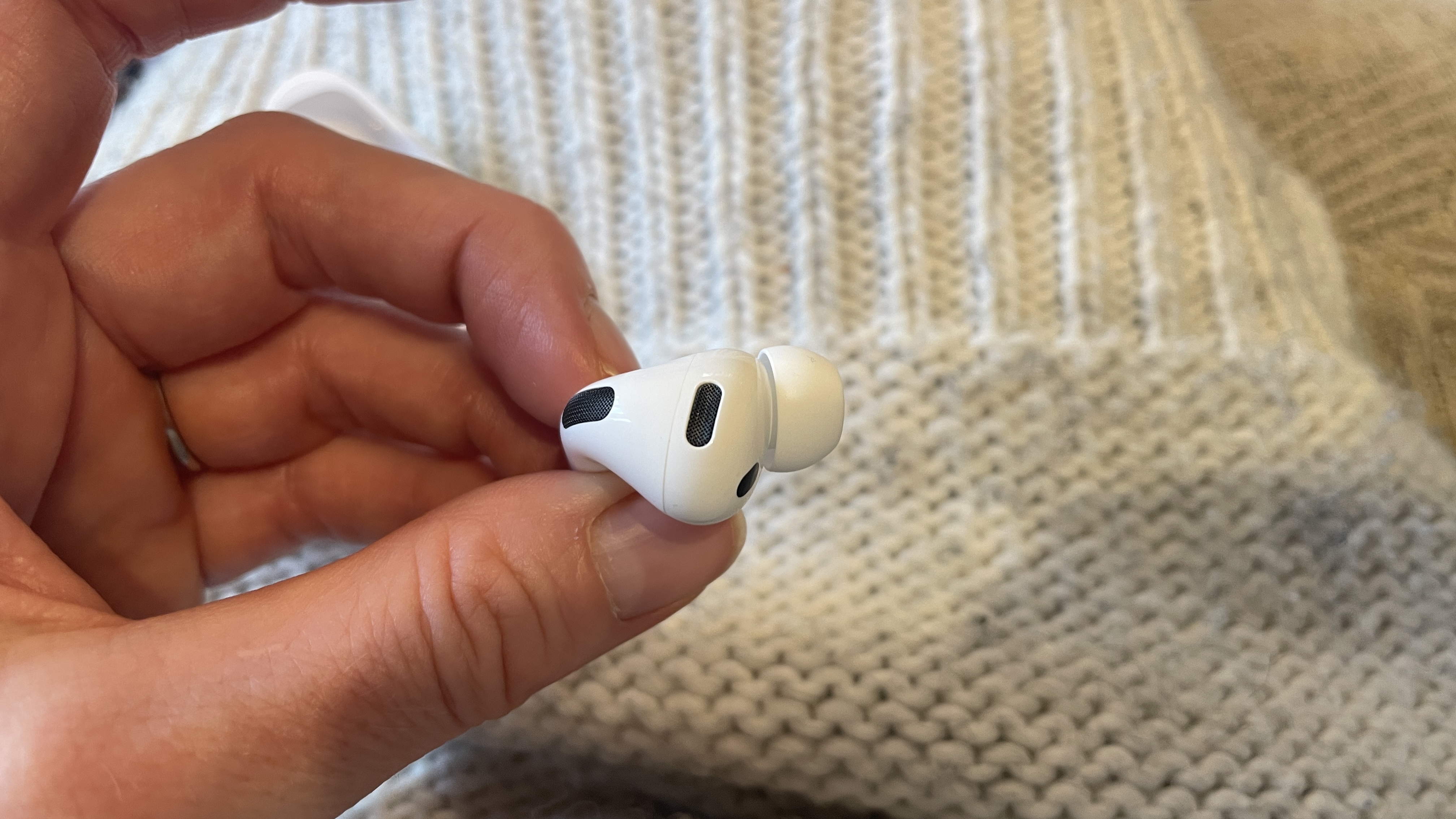 Apple AirPods Pro 3 held in a hand, with beige woollen background