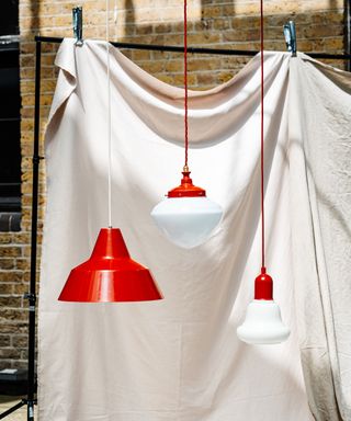 red and white pendant lights suspended in front of cream cloth in front of brick wall