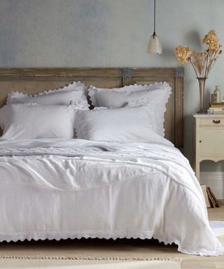 Violet 100% White Bed Linen on a bed against a gray wall.