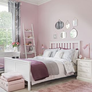 bedroom with pink wall white bed with designed cushions and frames on wall
