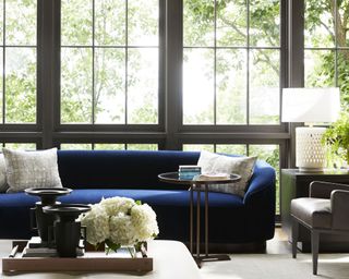 A blue sofa in front of large windows with a table lamp alongside.