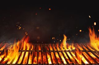 Flames underneath a grill with embers shooting off into the air against a black background.
