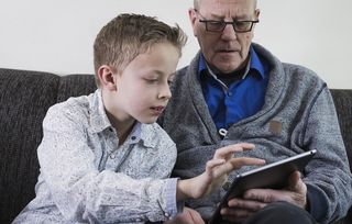 A man is shown how to work his iPad by his grandson.