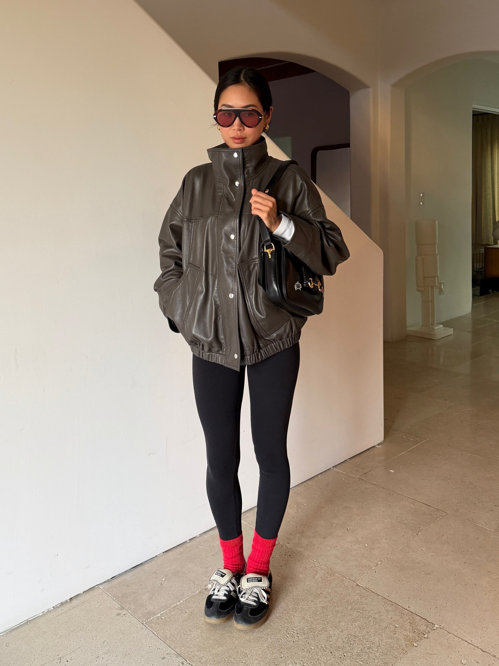 Influencer wearing a cinch-waist funnel-neck leather jacket, leggings, red socks, and black sneakers