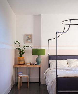 bedroom with white walls, pale pink lower half of walls, black bed frame, wooden table in corner with lamp and plant