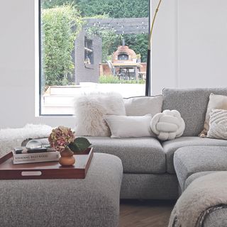 Living room with white walls, grey sofa and ottoman and large window.