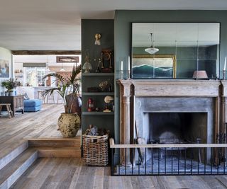 Fireplace framed in unvarnished wood with a rustic nasket of logs in an open plan living room/kitchen area