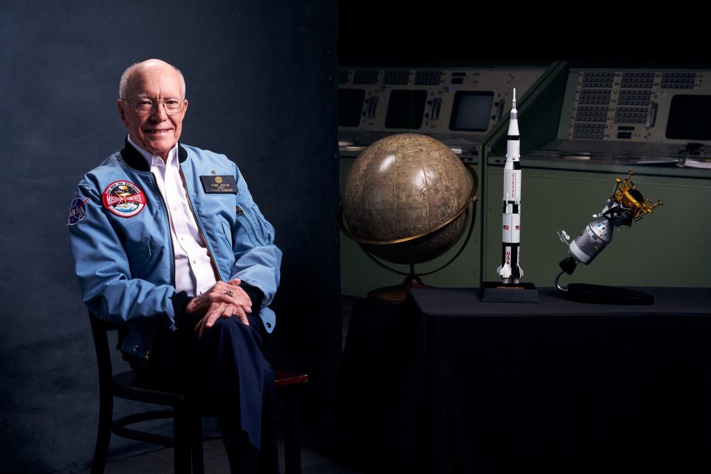 a man in a blue jacket sits beside spacecraft models