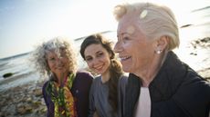 Three generations of adult women smiling at the beach.