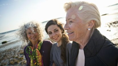 Three generations of adult women smiling at the beach.