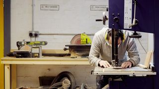 Man wearing ear protectors uses machine to cut a small piece of wood