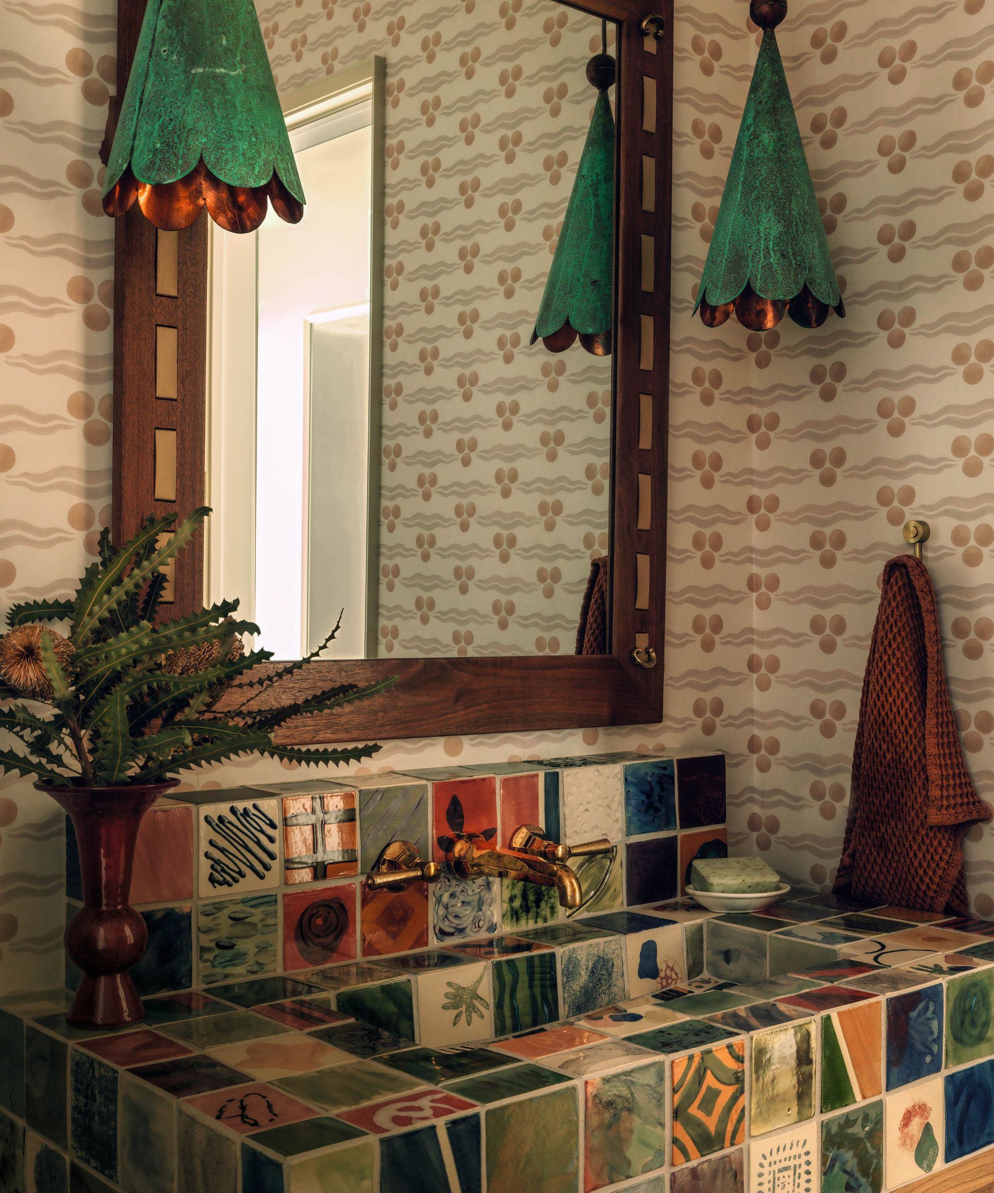 Powder room with statement tiled sink, wooden mirror, green pendant lights and patterned wallpaper