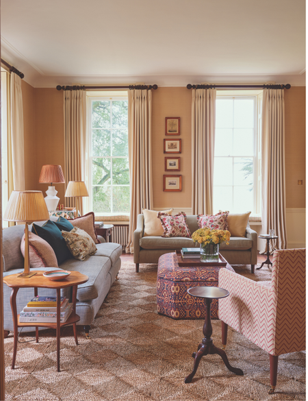 The cozy, pattern-filled living room of a 1700s country house restoration by Olivine Design, featuring an upholstered ottoman styled as a coffee table, holding a wooden tray of various objects.