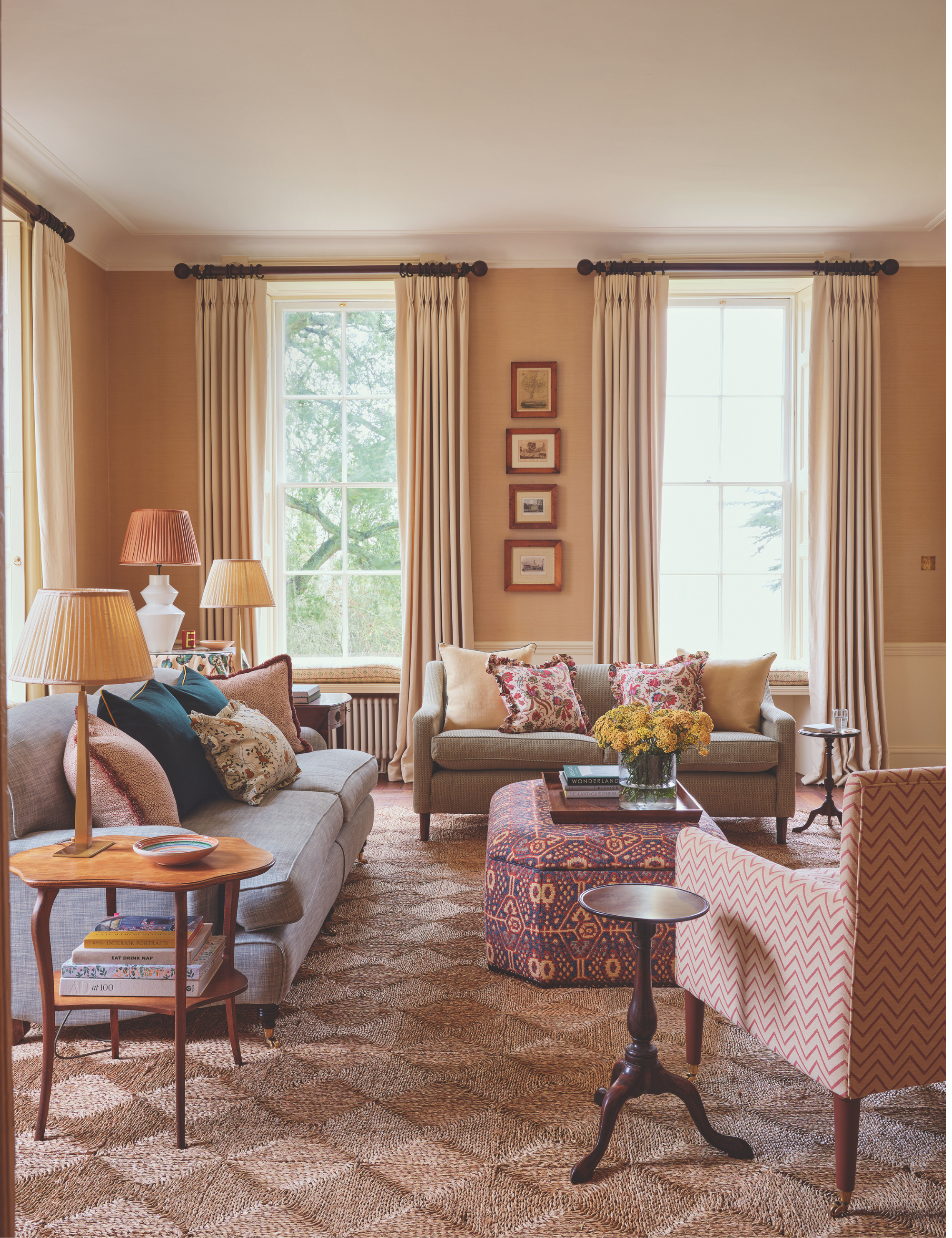 The cozy, pattern-filled living room of a 1700s country house restoration by Olivine Design, featuring an upholstered ottoman styled as a coffee table, holding a wooden tray of various objects.