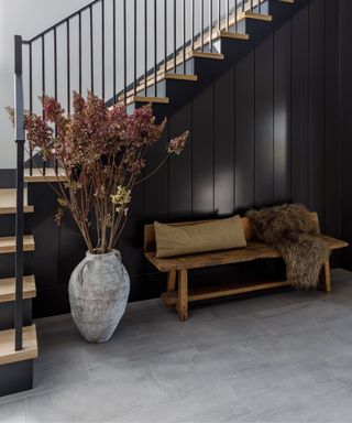 hallway with high gloss black panelling, contemporary iron railings and a rustic wooden shoe bench with a cushion and furry throw