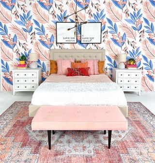 A bed with a pink and blue wall behind it, nightstands, and a bench in front of it