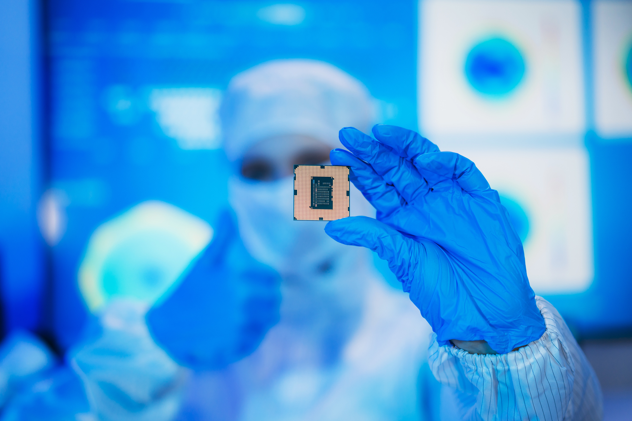 Professional technician inspecting a reflective semiconductor wafer inside a cleanroom at a semiconductor manufacturing plant, representing advanced microchip technology and quality control.