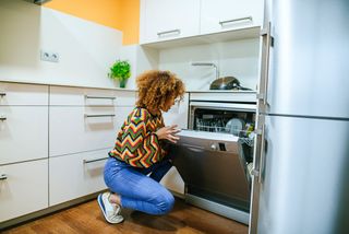 A woman opening a dishwasher in a light coloured kitchen