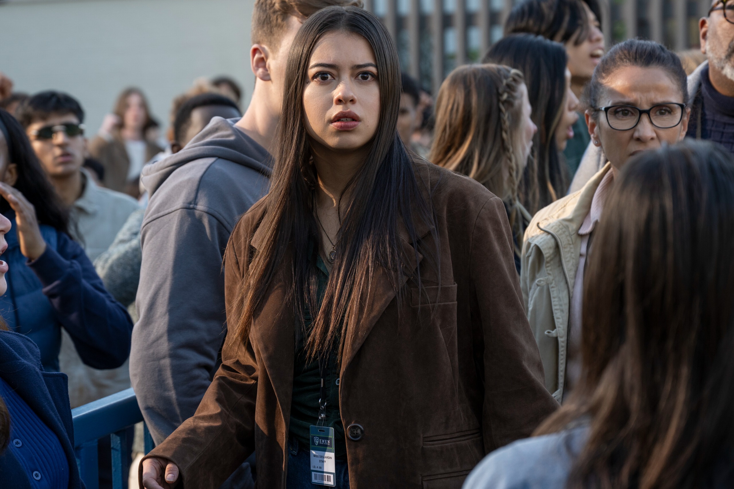 A woman in a brown jacket (Amber Midthunder as Rita Desjardin) stands in the middle of a busy crowd, in Prime Video's 'Carrie.'