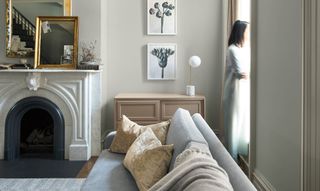 a modern Greige living room with white and wooden furnishings, and a woman standing in the window